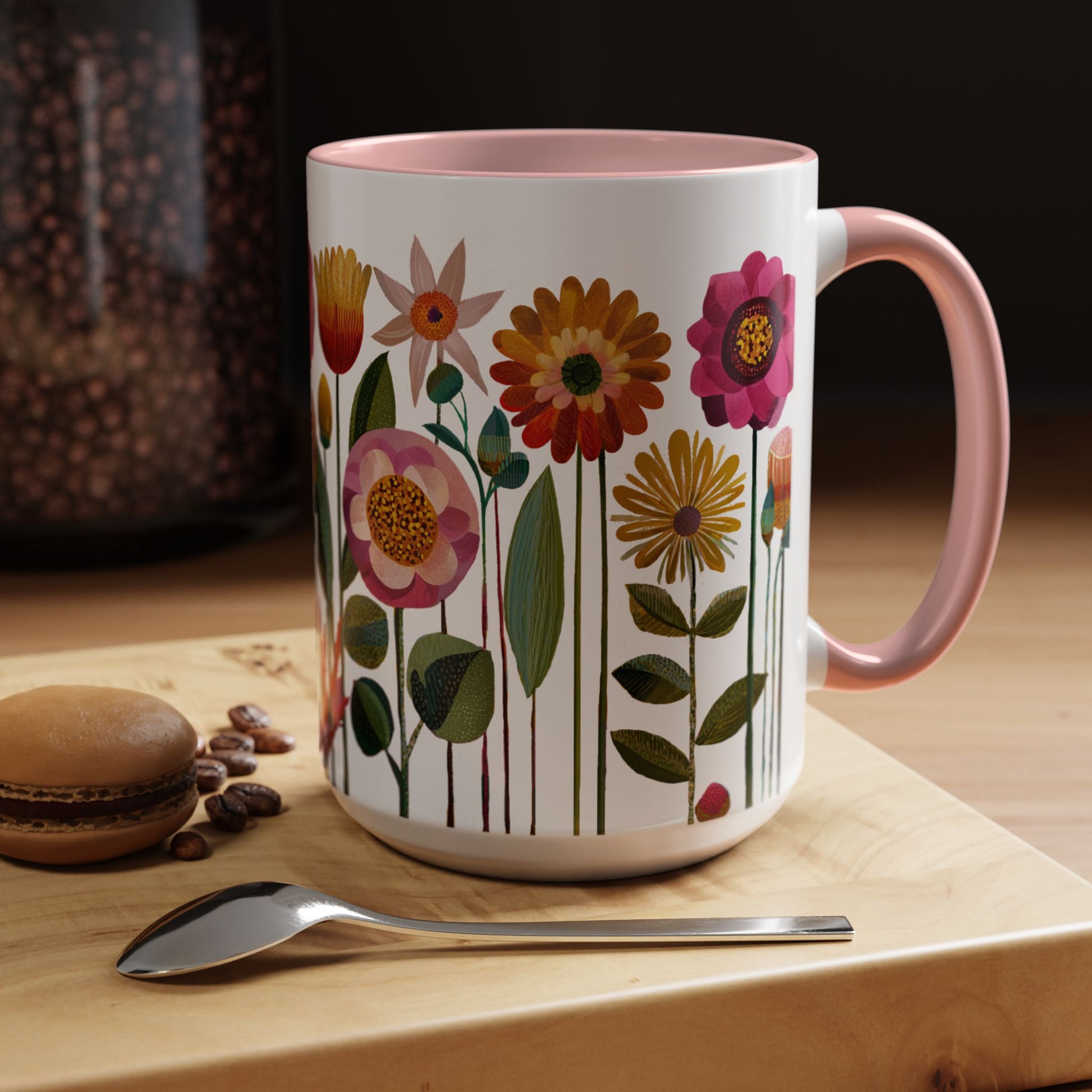 Floral-patterned mug with pink handle on a wooden surface with coffee beans and a macaron.