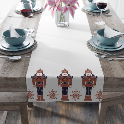 Table setting with a decorative table runner featuring nutcracker designs on a wooden table.