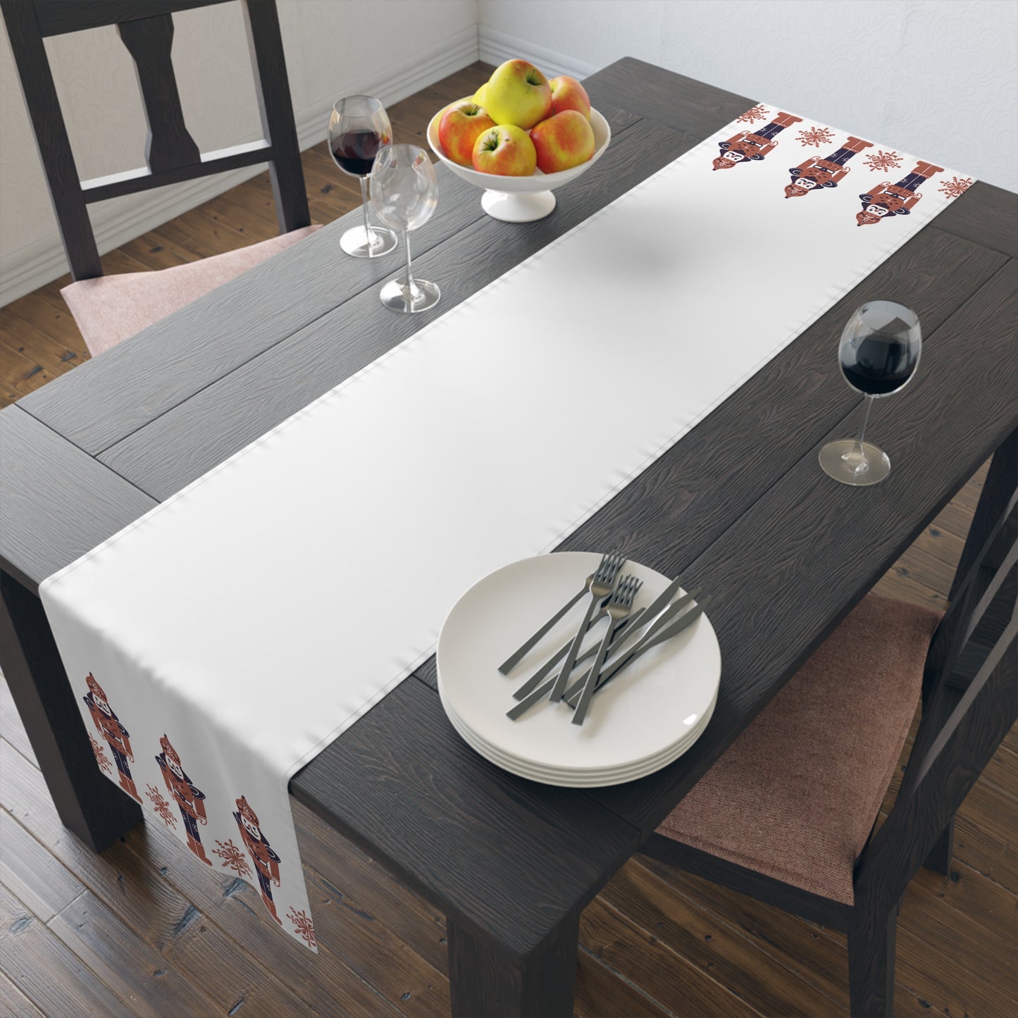 Dining table with a white CHRISTMAS themed runner, plates, forks, and a fruit bowl.