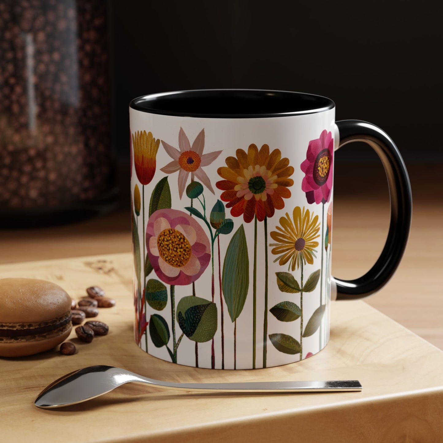 Mug with floral design, black interior and black handle  on a wooden surface with coffee beans and a spoon.