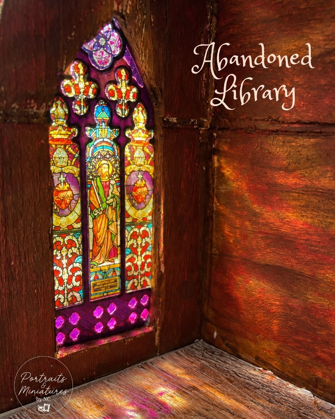 A miniature diorama model of an abandoned library corner, featuring a detailed stained glass window with a saint and warm amber light reflecting on the wooden walls and floor. White cursive text reads 'Abandoned Library' on the right.