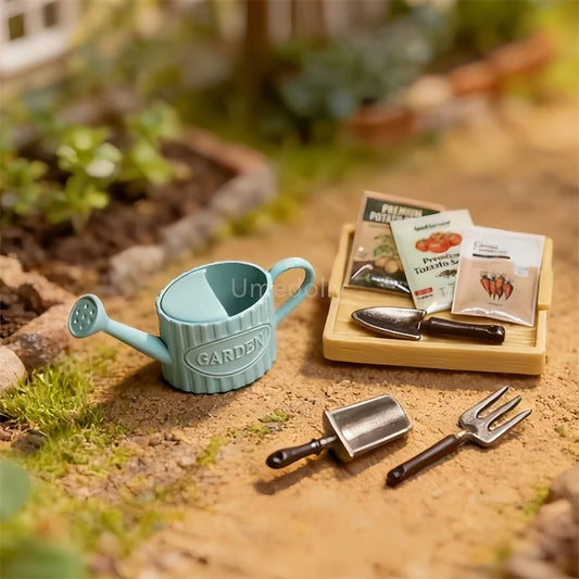 A miniature garden seed starter set displayed on sandy soil, featuring a light blue ribbed watering can, a small wooden tray holding seed packets and two metal trowels, with a blurred garden background.