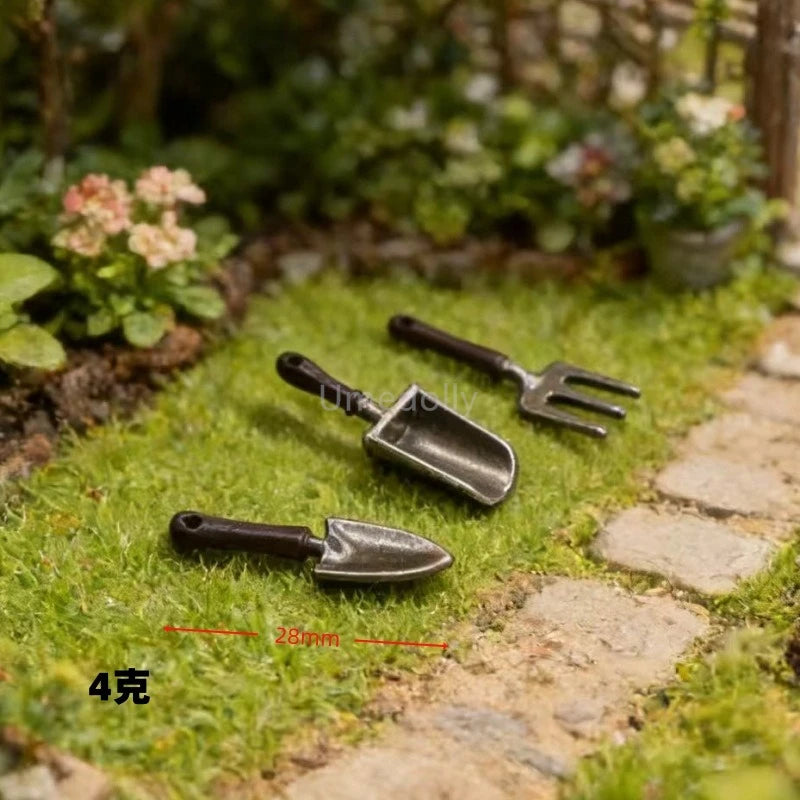 Three miniature garden tools with dark brown handles and dark gray metal heads are arranged on green grass beside a stone path. A red dimension line indicates the width of the trowel as 28mm, and the text '4g' appears in the lower left corner.