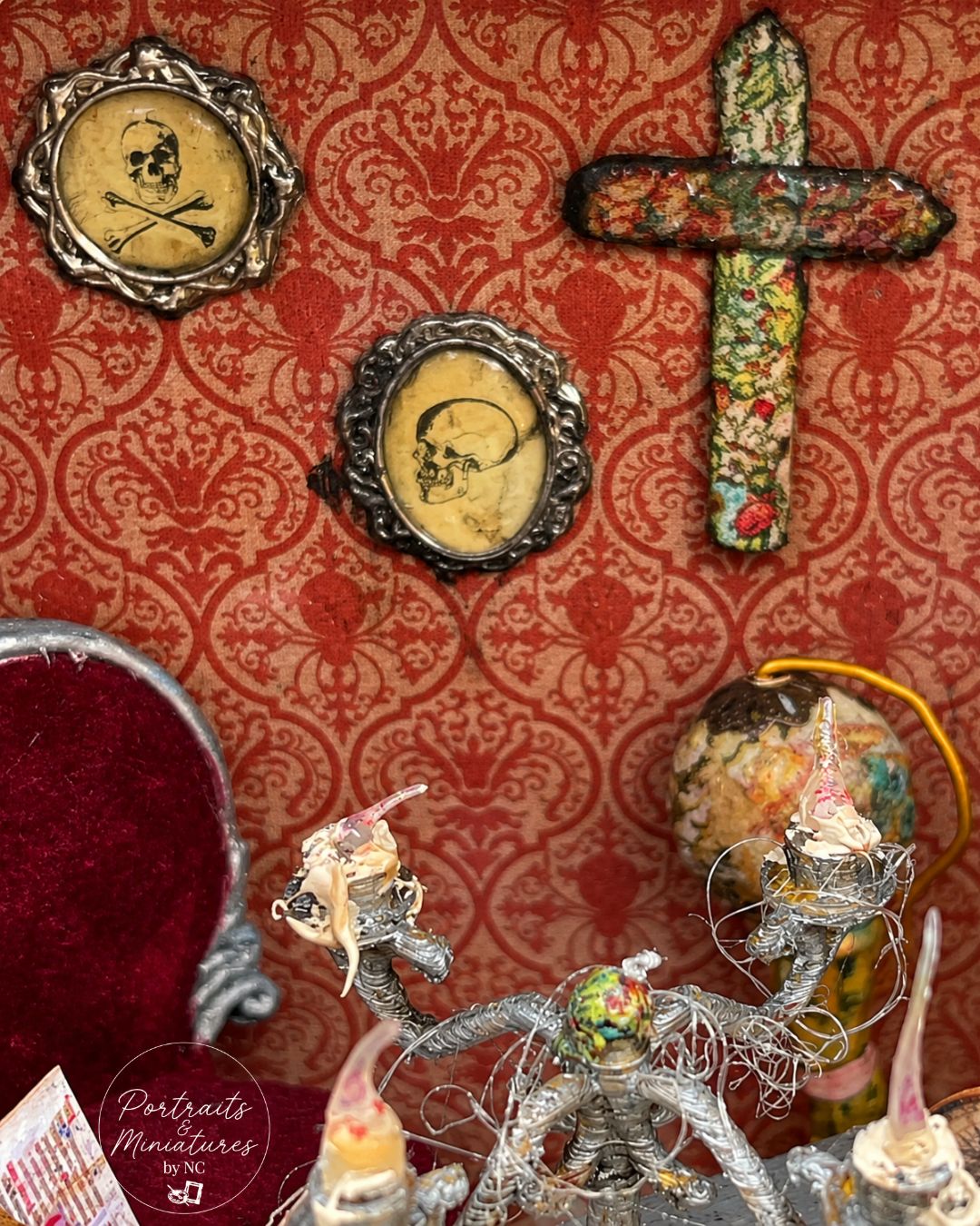 A collection of gothic and occult decorative items displayed against a red damask patterned background, including two skull portrait frames, a cross, a velvet mirror, and a silver skeleton figurine.