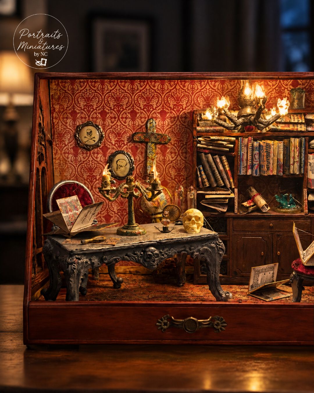 A detailed miniature diorama of a gothic study, featuring a small wooden cabinet with intricate miniature furniture, books, candles, and a skull, displayed on a wooden surface.