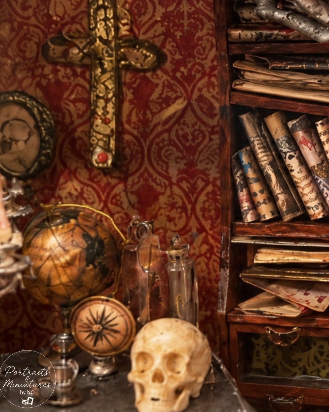A miniature diorama setup featuring a vintage skull, glass bottles, a globe, a compass, and a bookshelf filled with scrolls against a red damask wallpaper background.