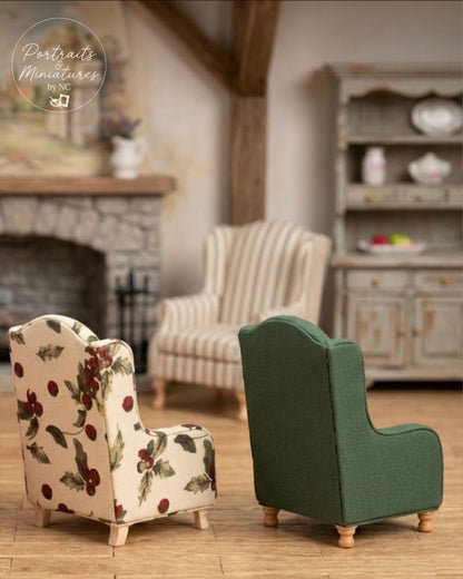 Two miniature armchairs for dolls displayed in a styled dollhouse living room setting. The foreground chair on the left features a cream fabric with a red berry and green leaf floral pattern, and the foreground chair on the right is upholstered in solid dark green fabric.