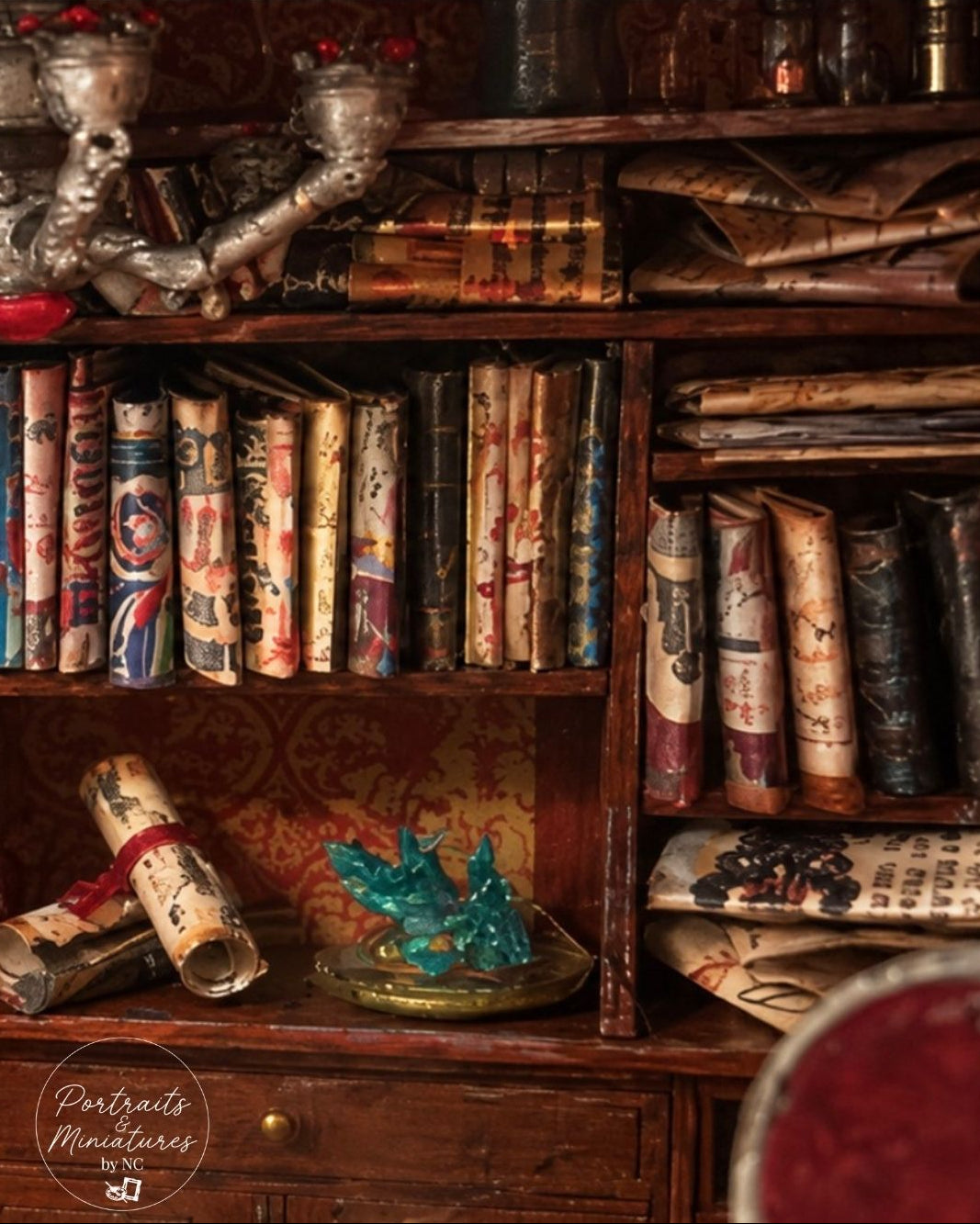 A dark wooden bookshelf filled with vintage-style books, scrolls, and decorative objects in warm brown, beige, and muted red tones. A turquoise crystal cluster sits on a tray on the lower shelf, and a circular 'Portraits & Miniatures' watermark appears in the bottom-left corner.